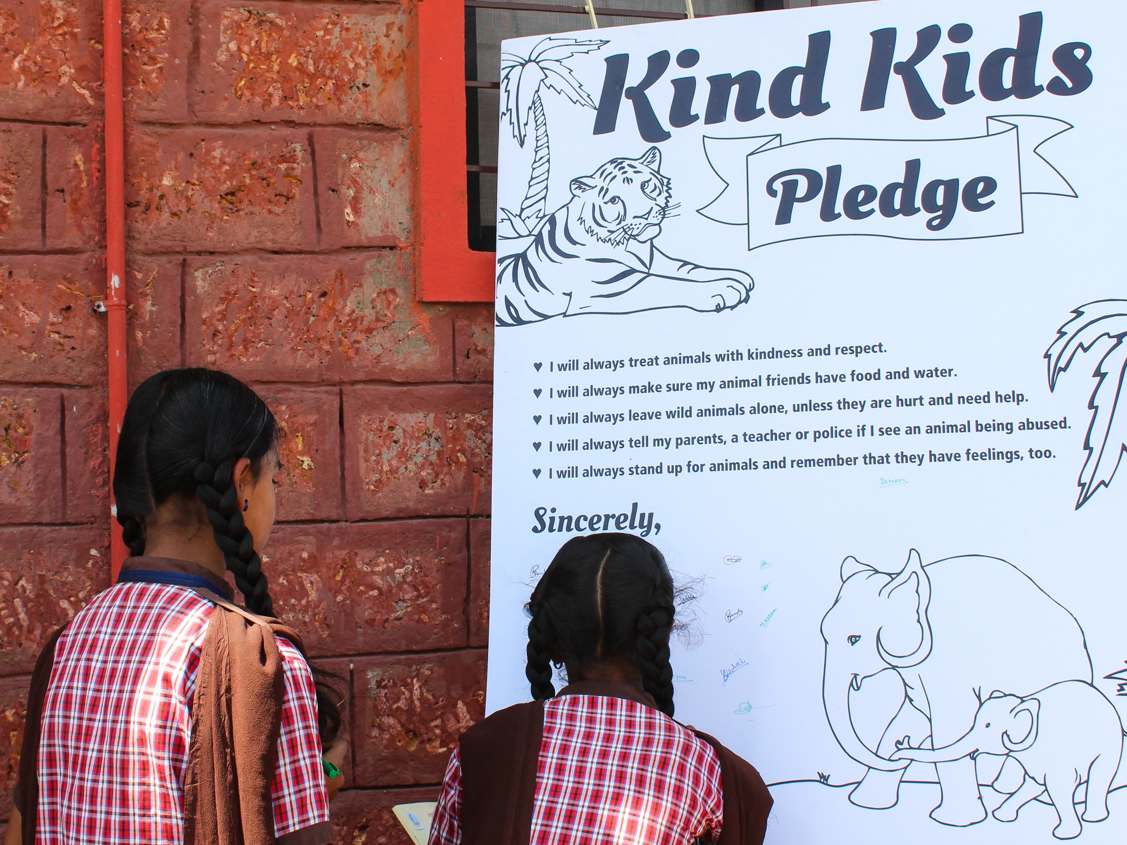 Two students sign their names to the "Kind Kids" pledge poster.