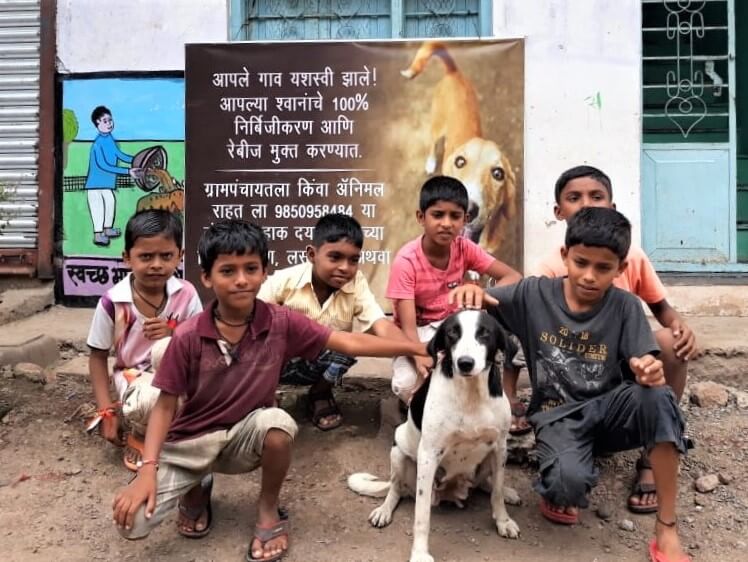 Children and one of the community's dogs smile for the camera in front of a banner announcing the village's recently earned 100% sterilization status.