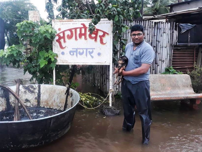 An Animal Rahat staff member stands in floodwater holding the puppy he just rescued.