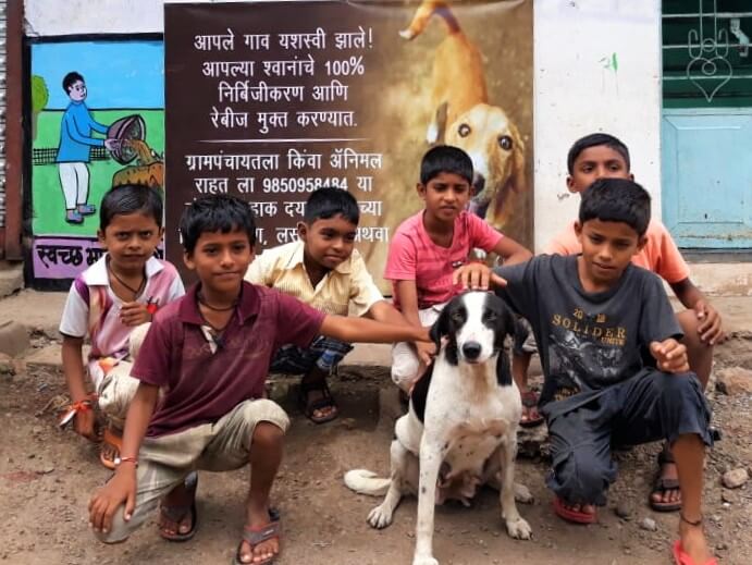 Children in Bavachi pose with a village dog in front of a banner celebrating the sterilization of 100% of the canines.