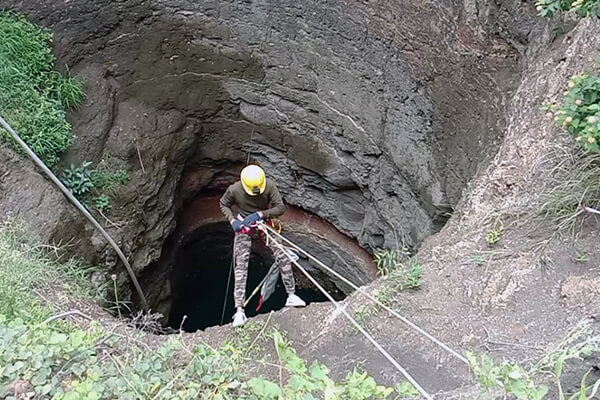 An Animal Rahat team member carefully avoids loose soil and mud at the top of the well as he rappels down to save the snake.