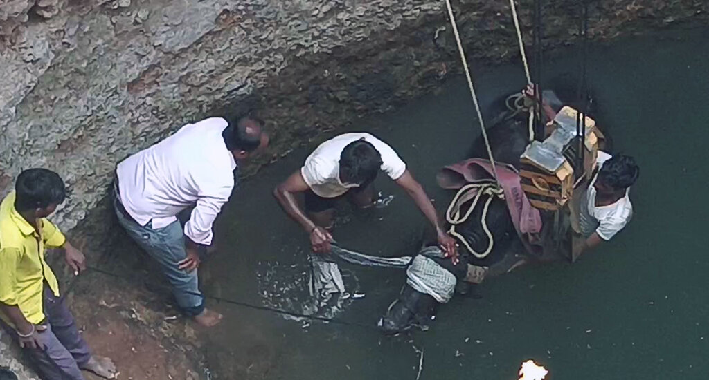 This image shows a water buffalo at the bottom of a well and Animal Rahat rescuers preparing to lift her out with a crane.